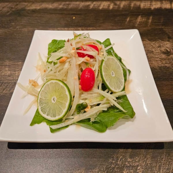 Erawan's Thai papaya salad with cherry tomatoes, lime slices, and peanuts on a white plate.
