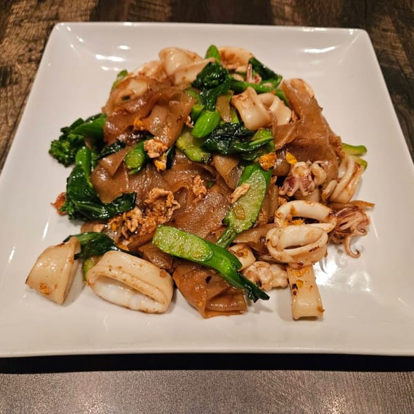 Erawan's Pad See Ew with wide noodles, squid, and green vegetables on a white plate.