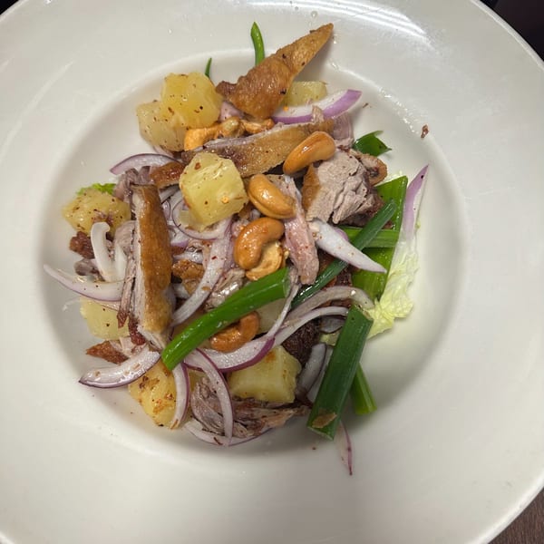 Erawan's Thai duck salad with pineapple, cashews, red onion, and green onions in a white bowl.