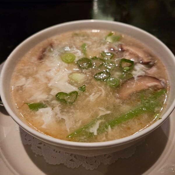 Close-up of Erawan's Thai soup with egg drops, mushrooms, and green onions in a white bowl.