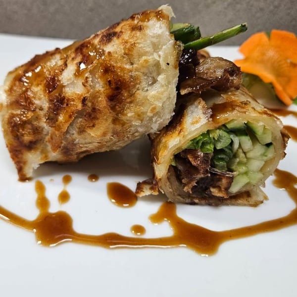 Two crispy Thai spring rolls, one cut open to show lettuce and cucumber, drizzled with sauce.