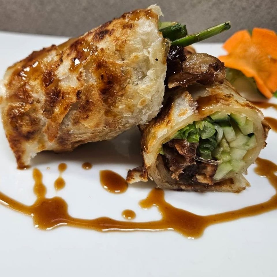 Two crispy Thai spring rolls, one cut open to show lettuce and cucumber, drizzled with sauce.