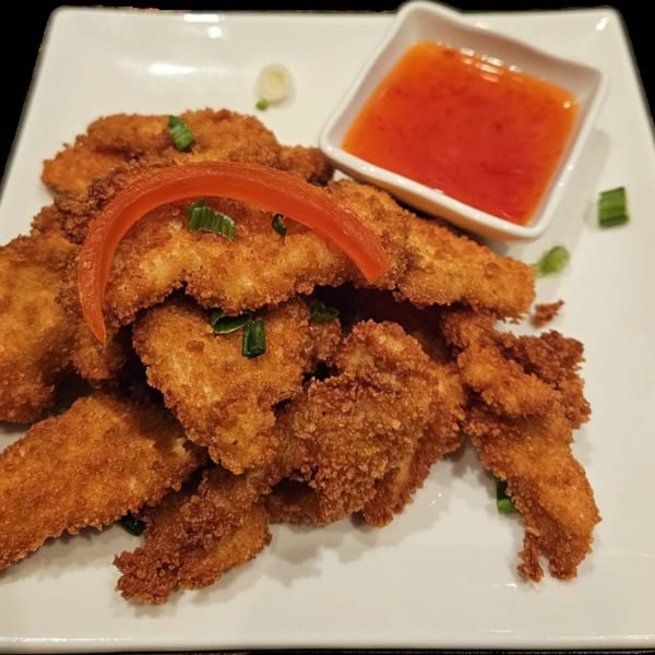 Crispy fried chicken pieces with a side of sweet chili dipping sauce on a white plate.