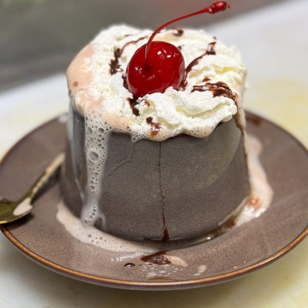 Chocolate dessert with whipped cream, chocolate drizzle, and a maraschino cherry on a brown plate.