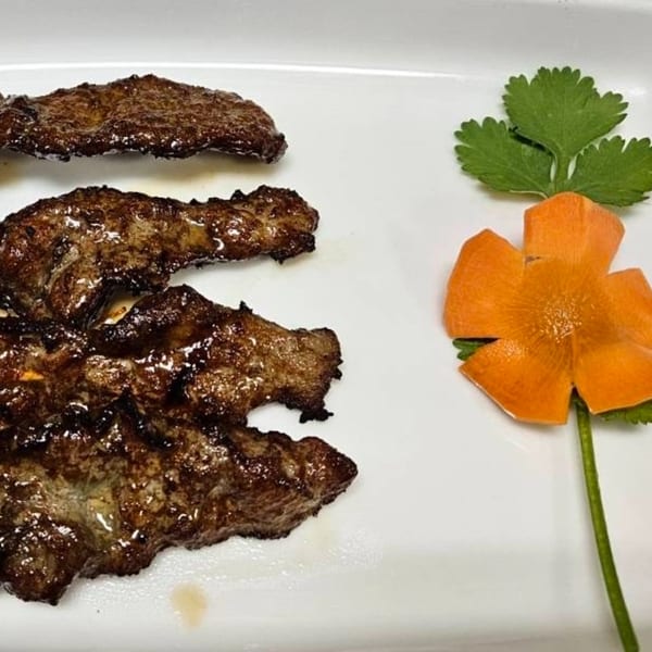 Grilled Thai beef slices with a decorative carrot flower and cilantro on a white plate.
