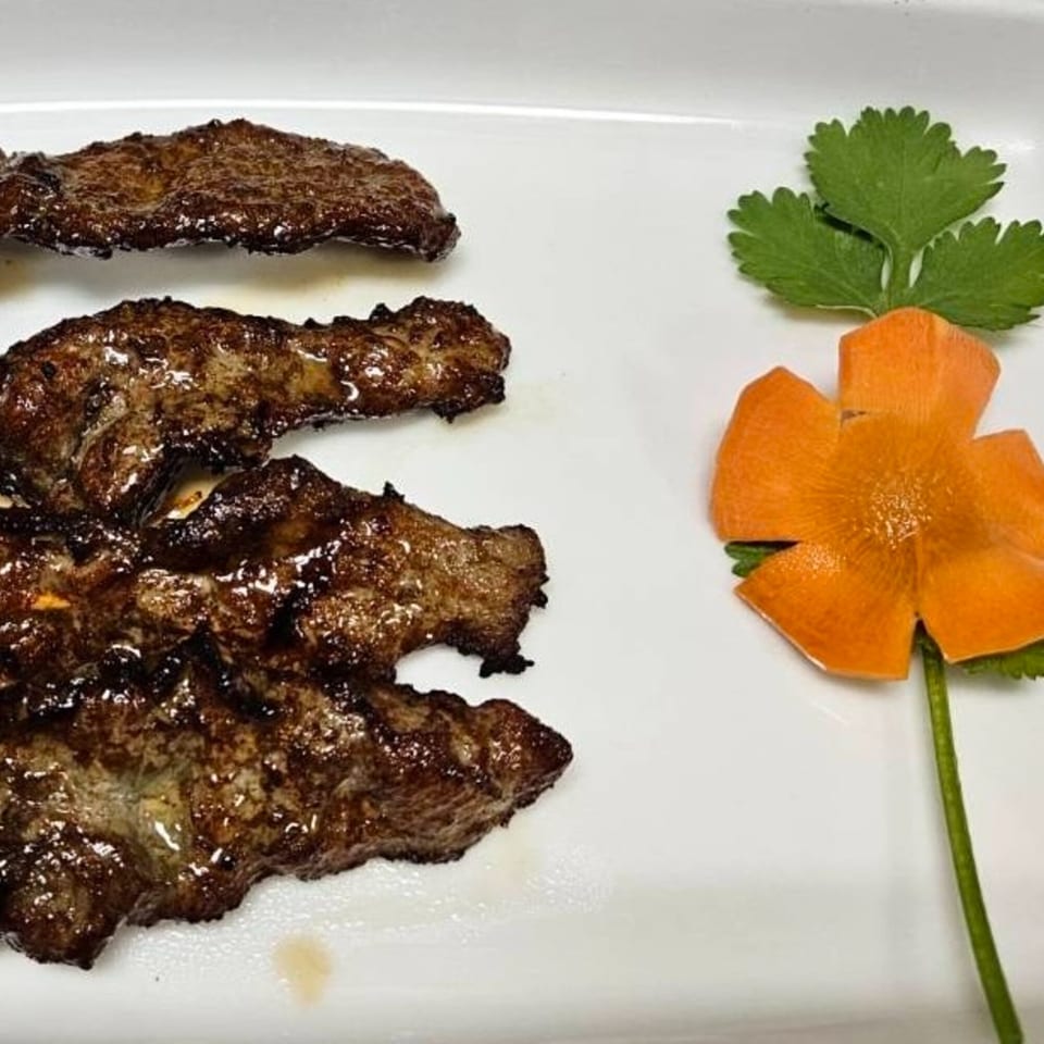 Grilled Thai beef slices with a decorative carrot flower and cilantro on a white plate.