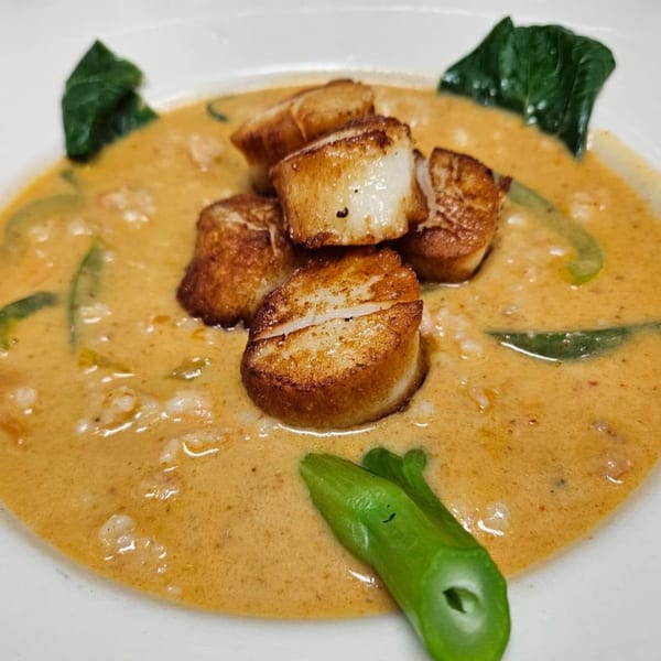 Pan-seared scallops in a creamy orange sauce with green vegetables in a white bowl.
