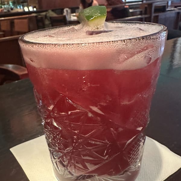 A vibrant red cocktail with a foamy top and lime garnish in a textured glass at Erawan.