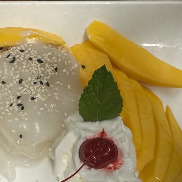 Erawan's mango sticky rice dessert with whipped cream, a cherry, and mint on a white plate.