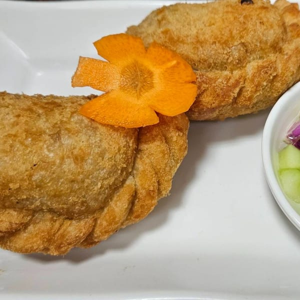 Two golden-brown fried Thai curry puffs, one garnished with a carved carrot flower, on a white plate.