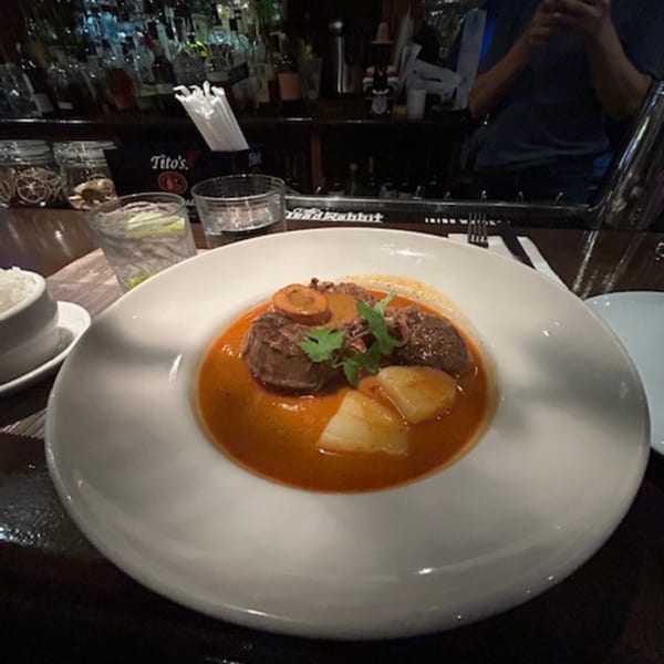 Erawan's Massaman curry with beef, potatoes, and carrots, garnished with cilantro, at a bar.