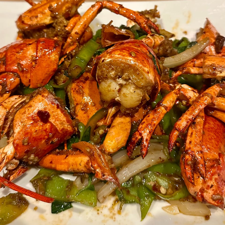 Close-up of a saucy seafood platter with lobster, crab claws, shrimp, peppers, onions, and greens.