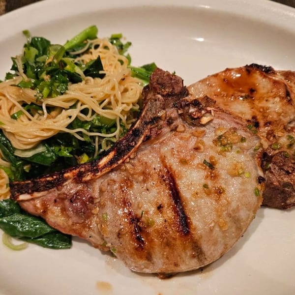 Grilled pork chops with noodles and green vegetables on a white plate at Erawan Thai restaurant.