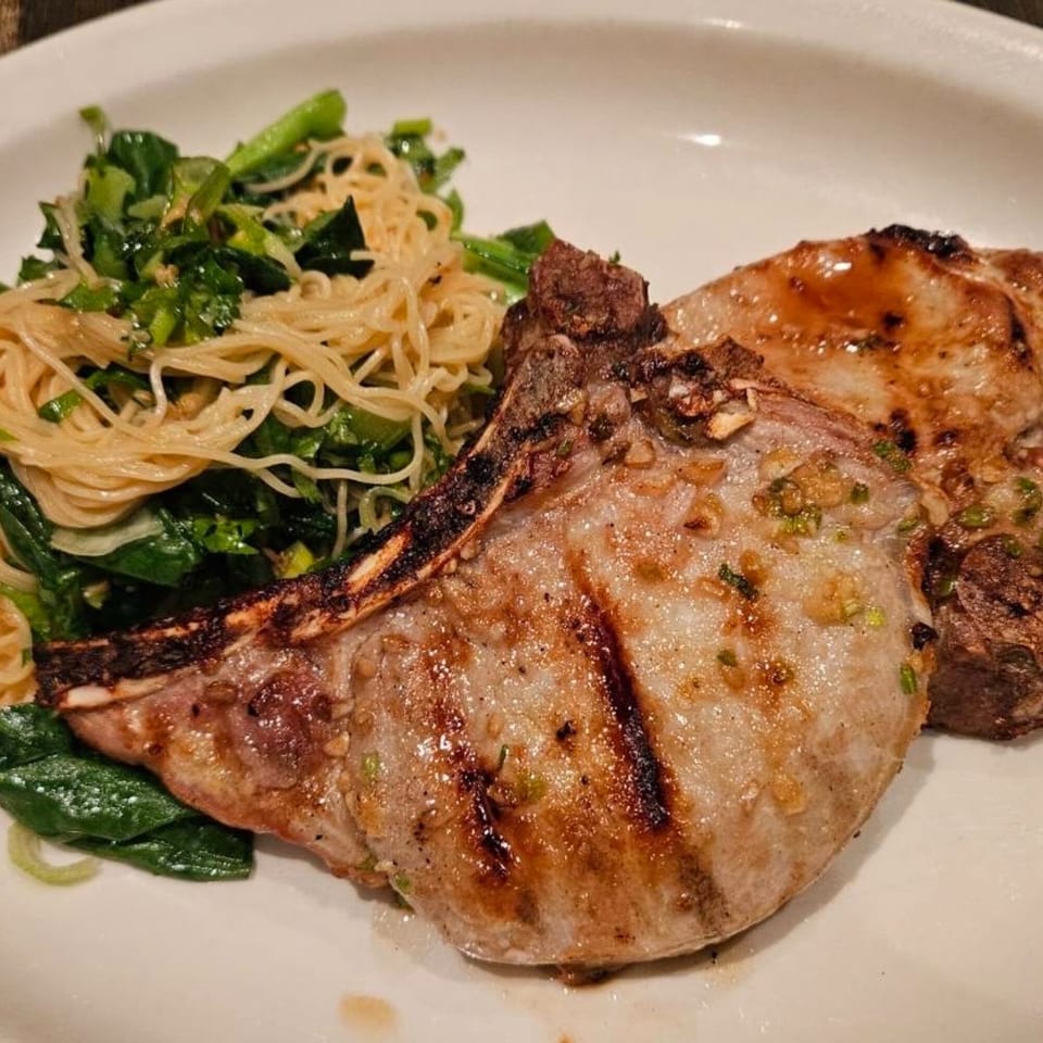Grilled pork chops with noodles and green vegetables on a white plate at Erawan Thai restaurant.