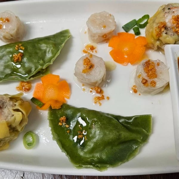 A white plate with various Erawan Thai dumplings, including green and white, garnished with carrots and scallions.