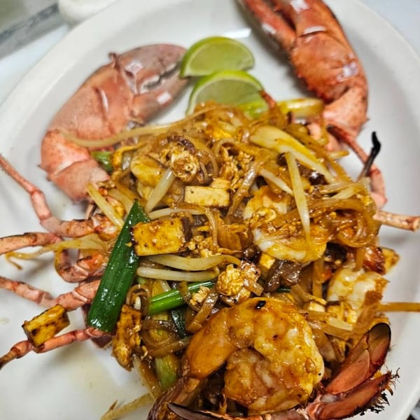 Erawan's Pad Thai with a whole lobster, shrimp, tofu, and lime wedges on a white plate.