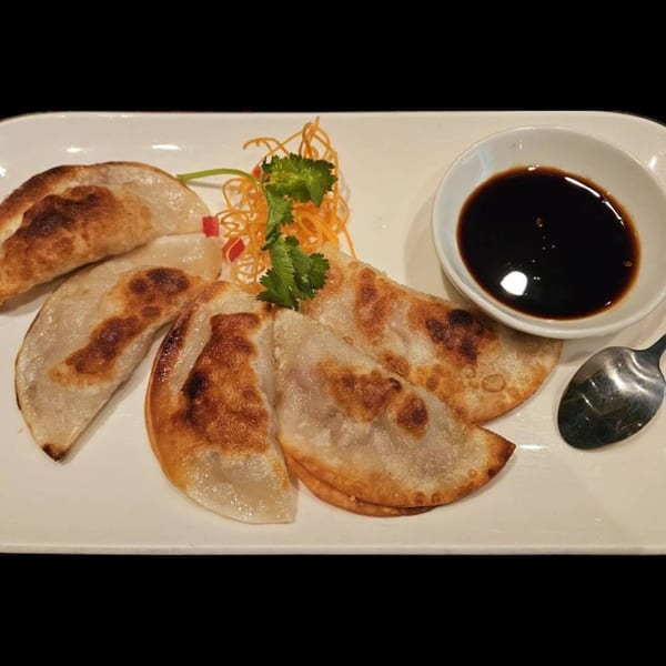 Pan-fried dumplings with a side of soy sauce, garnished with shredded carrots and cilantro.