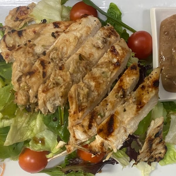 Grilled chicken slices on a bed of fresh lettuce with cherry tomatoes and a side of sauce.