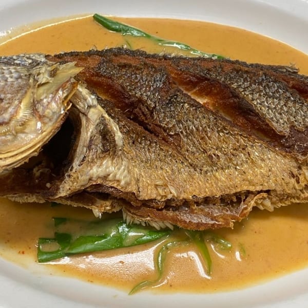 Crispy whole fried fish in a rich, creamy orange sauce with green vegetables on a white plate.