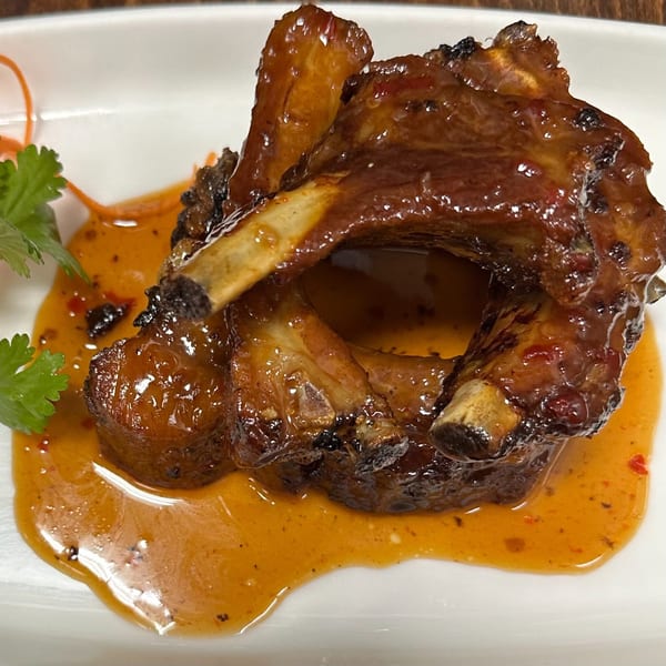 Erawan's Thai BBQ pork ribs, glistening with sauce, garnished with cilantro and shredded carrots.